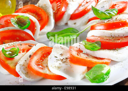 Préparés de fromage et salade de tomates en tranches en alternance de rouge et blanc garni d'herbes fraîches Banque D'Images