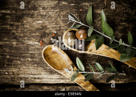 Cuillères en bois d'olivier avec olives fraîches et de feuilles sur une vieille table en bois texturé grungy avec copyspace Banque D'Images