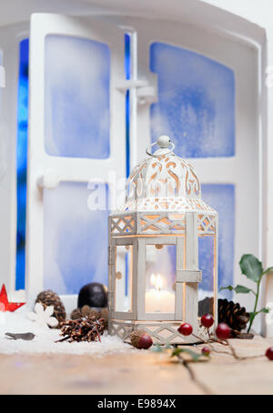 Joli Noël blanc lanterne avec une bougie allumée sur un rebord entouré par les cônes et les fruits décoratifs Banque D'Images