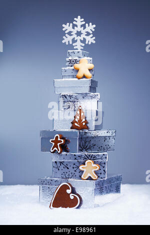 Pile de cadeaux de Noël aux couleurs fraîches dans la neige avec gingerbread cookies croustillants et un flocon illustrant la saison d'hiver Banque D'Images