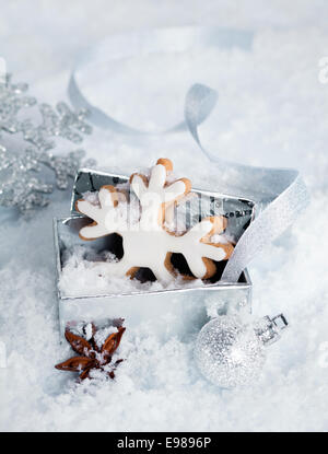 Biscuit flocon glacé de Noël dans une boîte-cadeau couché dans la neige entouré par d'autres décorations de fête et d'une épice badiane Banque D'Images