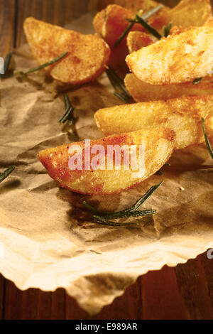 Golden au four ou quartiers de pommes de terre frites avec un revêtement épicé servi de repas à emporter sur papier brun avec feuilles de romarin Banque D'Images