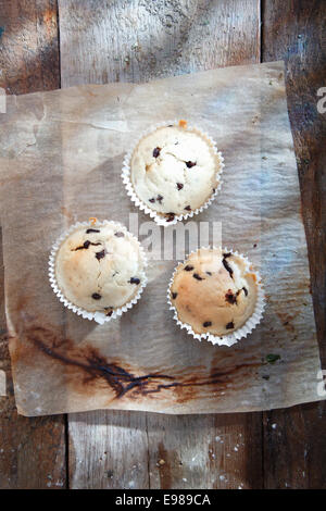 Vue de dessus de trois des petits muffins aux bleuets sur un refroidissement grungy feuille de papier four utilisé Banque D'Images