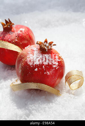 Grenades rouges mûres de fête avec du ruban d'or de décoration nichée dans la neige fraîche avec copyspace pour vos voeux de Noël Banque D'Images
