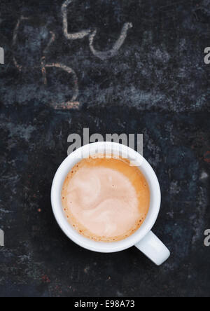 Vue aérienne d'un mousseux aromatique tasse de Cappuccino fraîchement infusé, debout sur un vieux tableau noir ardoise avec grungy griffonnages de craie et copyspace Banque D'Images