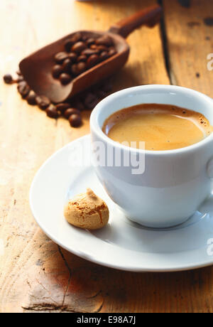 Café espresso aromatique fort servi dans une petite tasse avec un macaron sur le côté et une boule de grains de café dans l'arrière-plan Banque D'Images