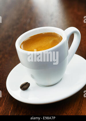 Une pleine tasse de café blanc avec un seul grain de café sur la soucoupe, sur un fond de bois foncé Banque D'Images