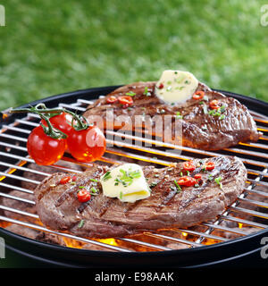 Partie de délicieux steak maigre surmonté avec le beurre et les herbes grillées sur un barbecue sur rouge les tisons en plein air sur la pelouse Banque D'Images