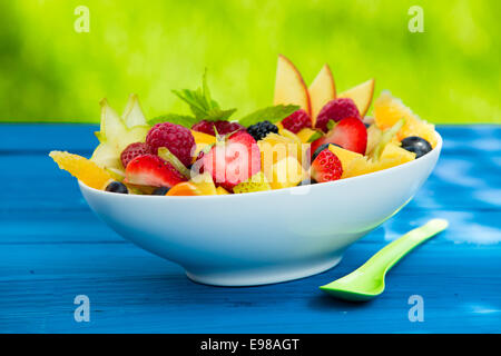 Mélange de morceaux de délicieux fruits frais dans un bol, sur une table contre un fond vert Banque D'Images