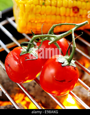 Trois tomates cerises rouges mûrs encore attaché à la vigne en équilibre sur une grille Barbecue Cuisson au-dessus d'un feu Banque D'Images