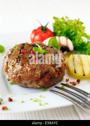 Burger de boeuf cuit succulent avec pomme de terre et de salade sur une assiette blanche. Banque D'Images