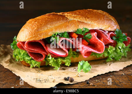 Baguette garnie d'or fraîchement rempli de laitues fraîches et fines tranches de salami assaisonné d'épices sur papier brun froissé Banque D'Images