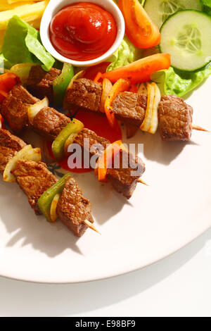 Brochettes de boeuf grillé avec des poivrons servi avec du ketchup , frites et salade fraîche sur une plaque blanche, high angle view Banque D'Images