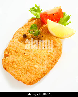 Vue rapprochée de la surface d'un doré croustillant poêlé escalope de veau en chapelure avec le citron, la tomate et le persil sur un fond blanc Banque D'Images