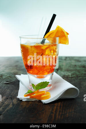 Servant d'Aperol spritz cocktail avec de la glace garnie de feuilles de menthe et de zeste d'orange sur une serviette pliée sur un vieux comptoir en bois dans un bar ou club Banque D'Images