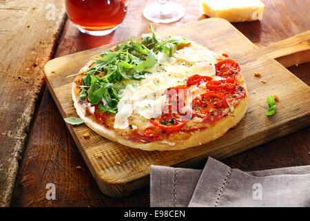 Pizza italienne coloré dans les couleurs nationales vert frais garni de feuilles de roquette, copeaux de fromage blanc et rouge des tomates dans trois bandes debout sur une planche de bois sur une vieille table rustique Banque D'Images