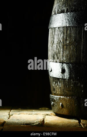 Old oak barrel debout sur dallage ou vieux briques avec un fond sombre et copyspace du vieillissement conceptuel et le stockage de vin, bière ou eau-de-vie Banque D'Images