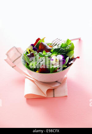 Chaque portion de salade d'herbes fraîches avec des fleurs de capucines dans un bol en porcelaine servi comme accompagnement d'un repas sur une serviette de table blanc Banque D'Images