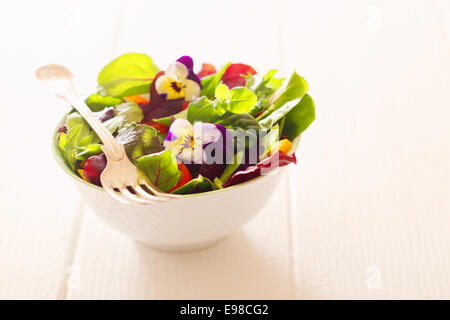 Salade d'herbes fraîches de la ferme en bonne santé avec des légumes-feuilles et fleurs de capucines servi dans un bol blanc avec une fourche sur un tableau blanc en bois Banque D'Images
