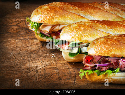 Trois baguettes savoureuses avec des obturations savoureux alignés sur un comptoir en bois rustique avec du rosbif et roquette, figues et fromage, salade et poulet et fourrages Banque D'Images