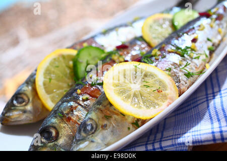 Close-up de trois sardines grillées avec des tranches de citrons sur un plateau sur une table à l'extérieur Banque D'Images