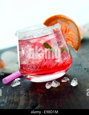 Cocktail daiquiri glacé servi dans un tumbler garni d'orange sur un comptoir de bar en bois Banque D'Images