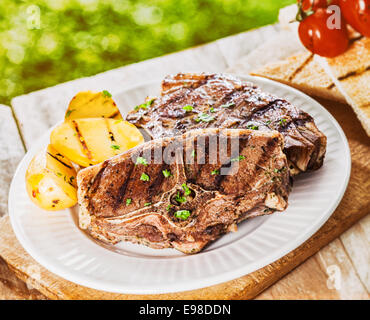 Côtelettes d'agneau maigre sain avec des pommes de terre grillées servies à un barbecue en plein air sur une table de pique-nique en bois rustique pour un petit-déjeuner nutritif Banque D'Images