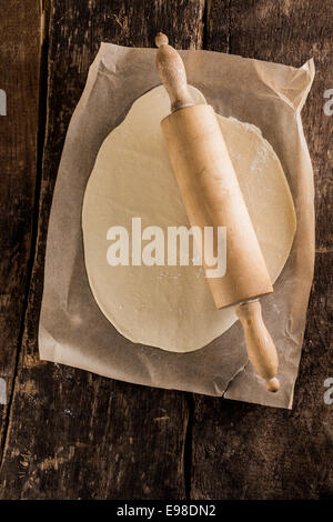 Préparation de la base d'une pizza italienne avec une vue de dessus de la pâte roulée sur four papier avec un rouleau à pâtisserie en bois sur une table de cuisine en bois rustique Banque D'Images