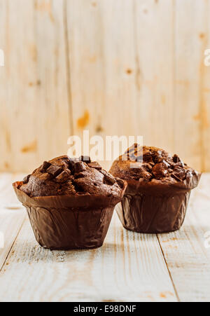 Deux des petits muffins aux pépites de chocolat savoureux dans des gobelets en papier brun debout sur une table en bois haut dans une cuisine rustique avec un fini grain de bois et copyspace Banque D'Images