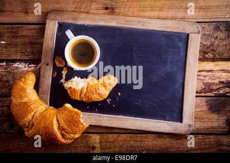 Vue de dessus d'une tasse de café et un croissant feuilleté brisé en deux sur une ancienne école sur une ardoise en bois rustique, de fond copyspace sur l'ardoise Banque D'Images