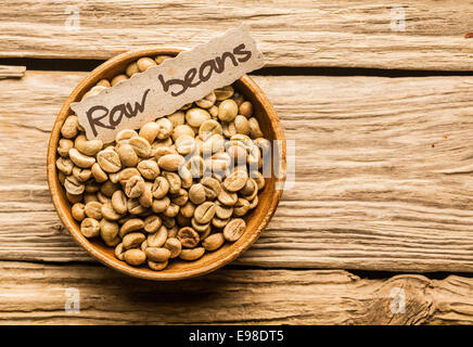 Bol de café en grains crus sur une vieille table en bois Banque D'Images