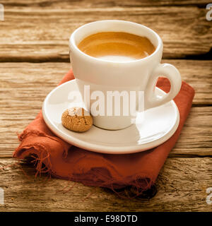 Délicieuse tasse de café expresso fraîchement préparé servi dans une tasse et soucoupe blanc ordinaire avec un macaron sur une surface rustique en bois patiné grungy, Close up format carré Banque D'Images