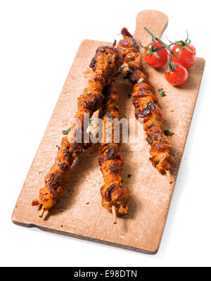 Trio de brochettes de viande grillées épicées nutritif servi sur une vieille planche en bois avec un rôti tomates cerise, isolated on white Banque D'Images