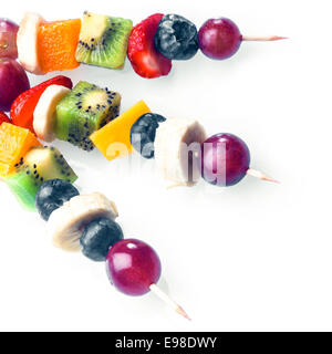 Trio de brochettes de fruits tropicaux colorés disposés en éventail avec raisins, kiwis, fruits rouges, orange et banane sur fond blanc avec copyspace, format carré Banque D'Images