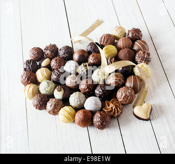 Close-up of a heart shape réalisés avec différents types de truffes au chocolat décoré d'un ruban d'or bouclés sur une table en bois blanc Banque D'Images