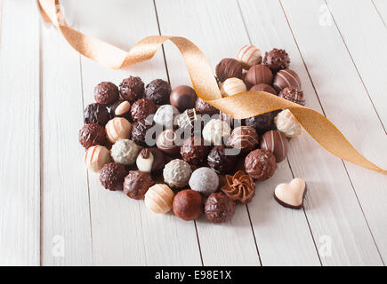 Forme de coeur fait avec divers types de truffes au chocolat décoré d'un ruban d'or sur une table en bois blanc Banque D'Images