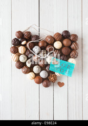 Forme de coeur fait avec divers types de truffes au chocolat et une étiquette bleue avec un message romantique sur une table en bois blanc Banque D'Images