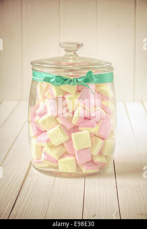 Low angle et vue rapprochée d'un vieux pot en verre rempli de bonbons carrés de guimauves rose et jaune et un ruban vert sur une Banque D'Images