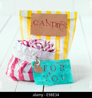 Close-up de deux sacs colorés avec blanc, jaune et rose remplis de bonbons avec un message romantique dans les étiquettes de sens, friandises pour vous, sur un fond de bois blanc Banque D'Images