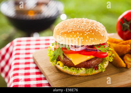 Délicieux cheeseburger avec fromage cheddar fondu dégoulinant sur le boeuf haché burger garni de salade fraîche ingrédients et servis sur une table de bois sur une table de pique-nique en plein air Banque D'Images