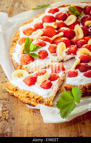 Délicieuse tarte aux fraises fraîchement cuits au four avec crème fouettée et garnir de tranches de banane sur un fond de tarte feuilletée dorée avec une seule tranche supprimé Banque D'Images