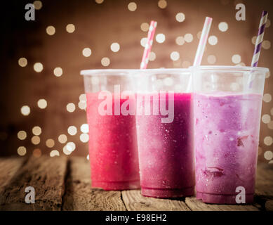 Trois couleurs différentes avec des smoothies berry lumières lumières parti debout dans une rangée sur un comptoir en bois rustique dans un restaurant ou bar Banque D'Images