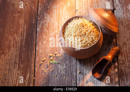 Boulgour ou blé concassé dans un pot en terre cuite utilisé dans la cuisine du Moyen-Orient, high angle view sur de vieux bois texturé avec copyspace Banque D'Images