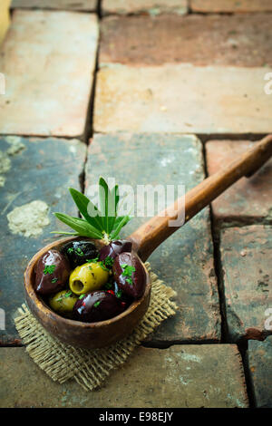 High angle view of assorted olives dans une louche en bois d'un bouquet de feuilles reposant sur de la toile de jute sur old weathered briques avec copyspace Banque D'Images