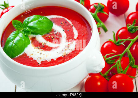 Les tomates fraîches avec de savoureux soupe aux tomates arrosées de crème et saupoudrée de poivre du basilic frais garni de Banque D'Images