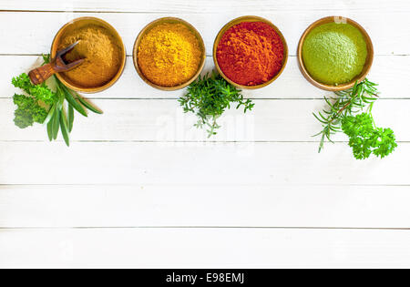 Les herbes culinaires et les épices colorés dans des bols en bois debout dans une ligne blanche sur les panneaux peints avec copyspace ci-dessous, overhead view Banque D'Images