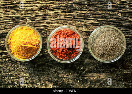 Vue supérieure de l'ouverture de trois conteneurs d'épices curry colorés, la poudre de chili ou poivre rouge sur un vieux fond de bois patiné vieilli avec copyspace Banque D'Images