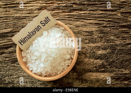 Les cristaux de sel de l'Himalaya, un sel de roche en provenance des mines au Pakistan, dans un bol avec un nom étiquette sur une surface en bois, texture grunge Banque D'Images