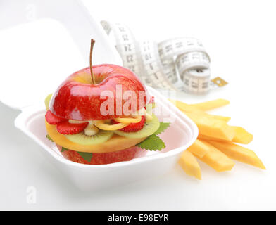 Apple burger sain dans un fast food à emporter contenant d'une juteuse pomme rouge fendit et rempli de dés de fruits tropicaux frais et de la sauce avec des matraques ou des chips de fruits et d'un ruban de mesure Banque D'Images