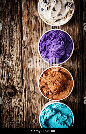 Sélection gastronomique de la crème glacée ou Yogourt glacé dans une variété de couleurs et de saveurs servi sur une table en bois rustique dans une rangée de cuves à emporter en plastique avec copyspace Banque D'Images